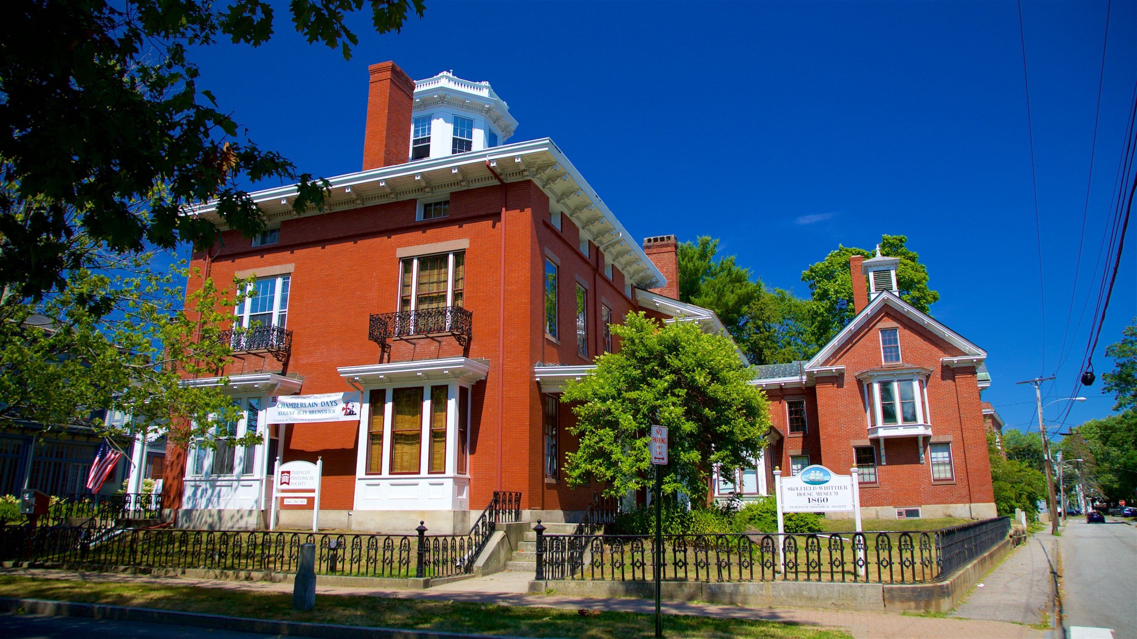 A historic red brick building with a white facade, a prominent chimney, and a balcony with wrought iron railings.