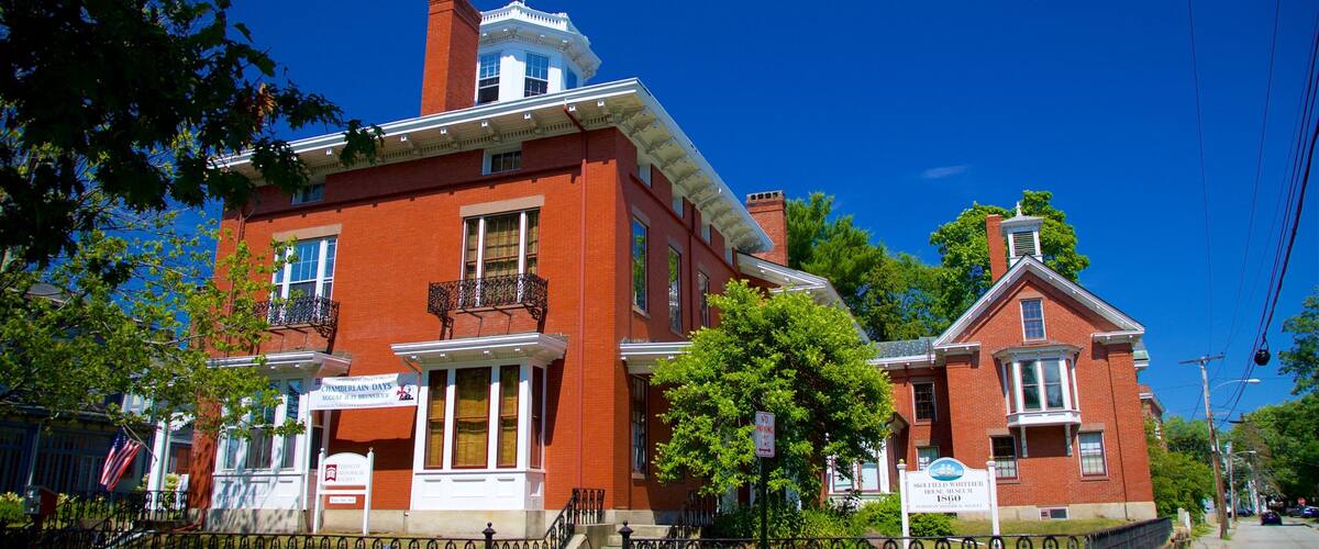 A historic red brick building with a white facade, a prominent chimney, and a balcony with wrought iron railings.