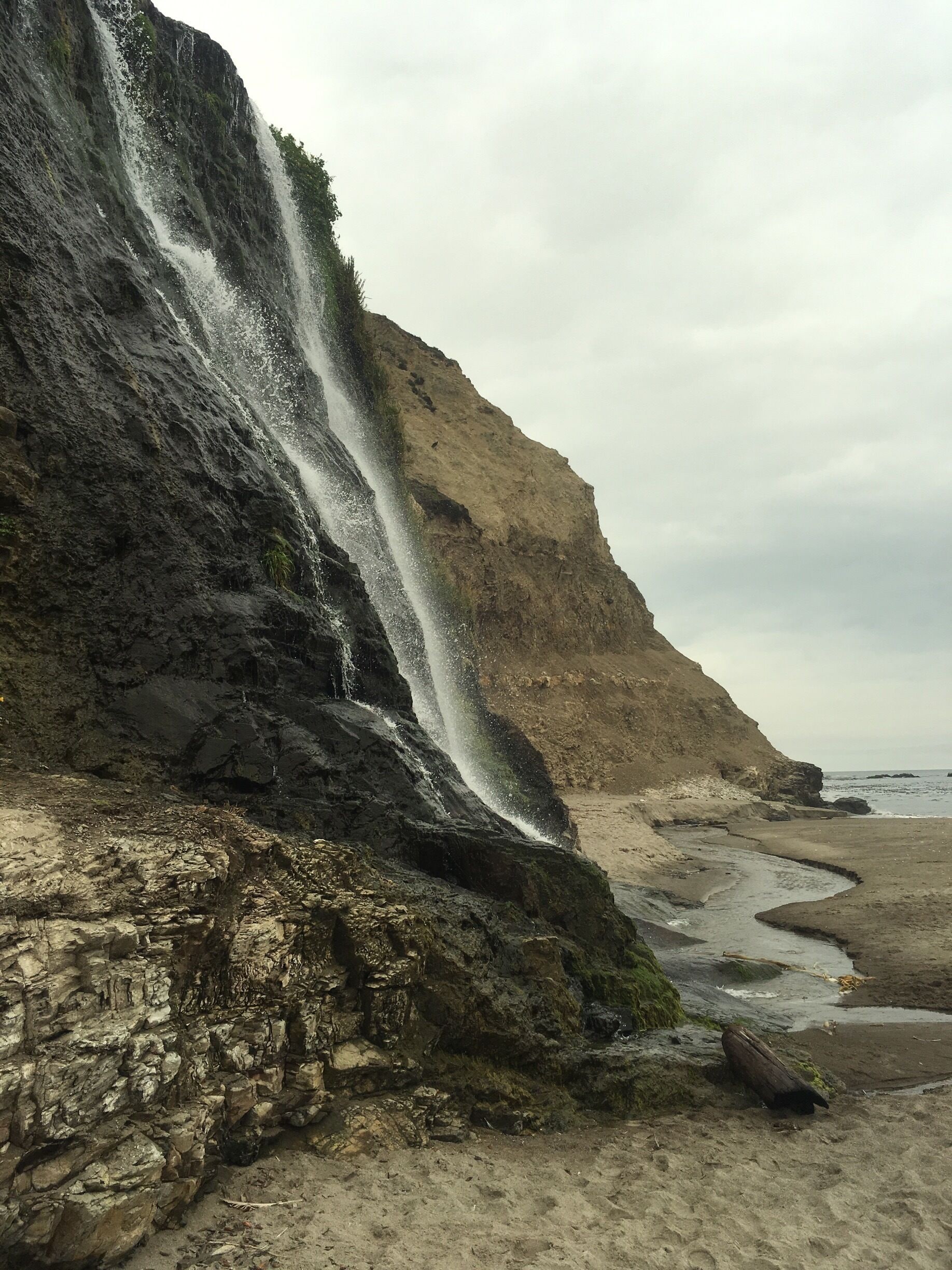 A waterfall cascading down a rocky cliff into a sandy beach area.