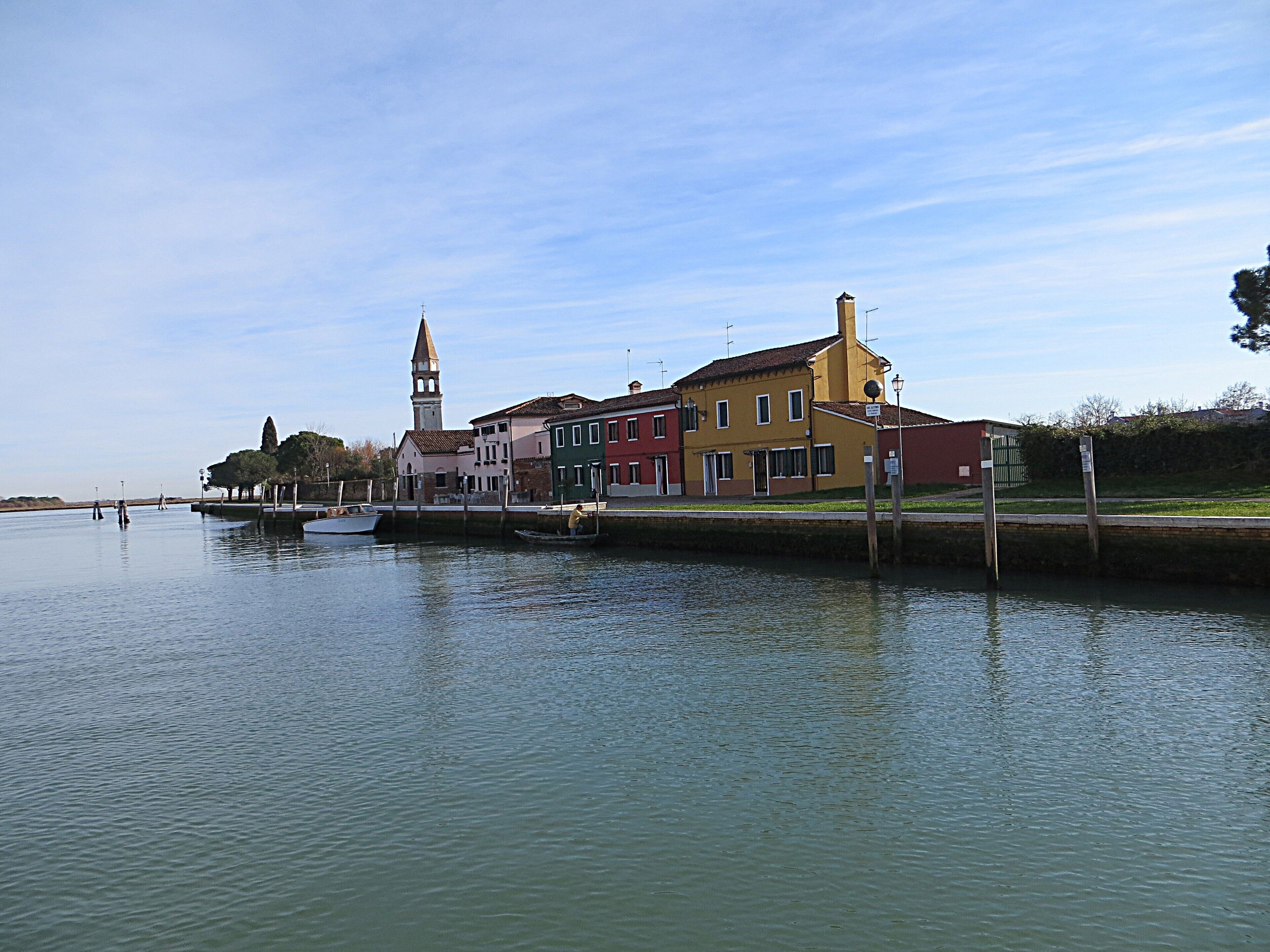 A canal with a row of colorful buildings, a boat docked on the left, and a tower in the background.