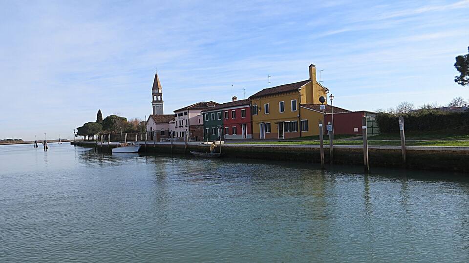 A canal with a row of colorful buildings, a boat docked on the left, and a tower in the background.