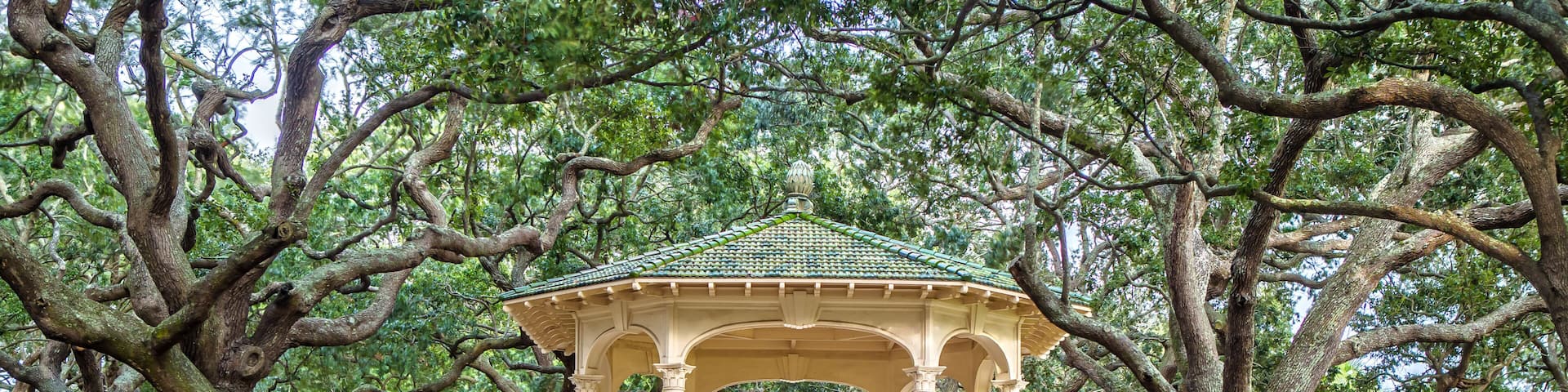 A gazebo with a green roof, surrounded by large trees in a park.