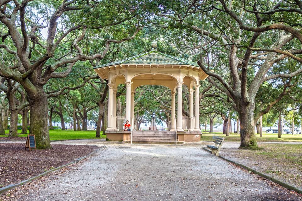 A gazebo with a green roof, surrounded by large trees in a park.
