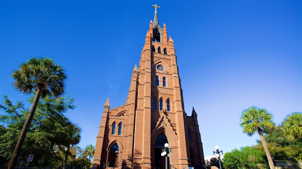 A tall brick church with a cross on top, surrounded by palm trees.