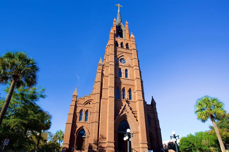 A tall brick church with a cross on top, surrounded by palm trees.