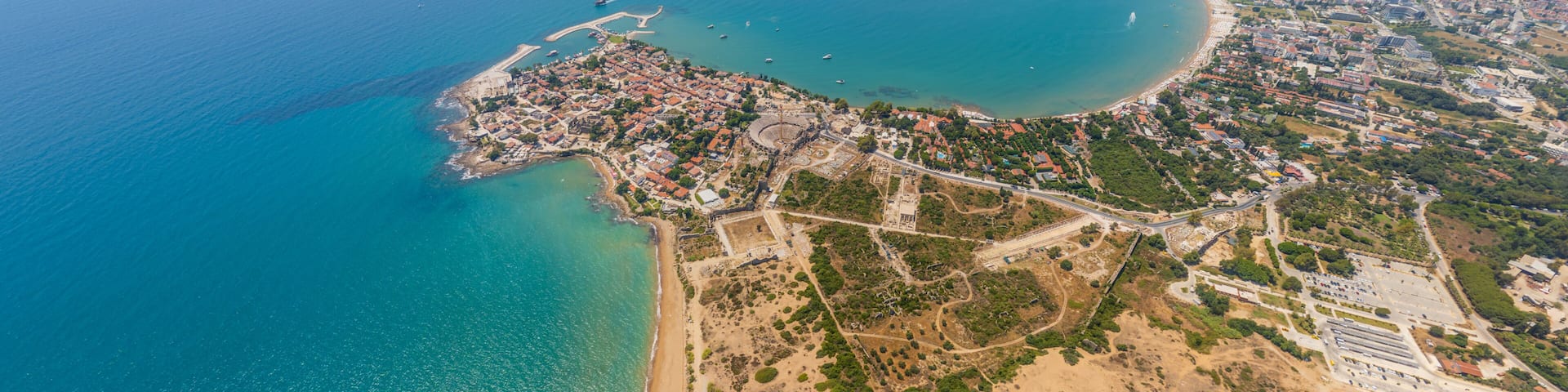An aerial view of a coastal city with a beach, a bay, and surrounding urban areas.
