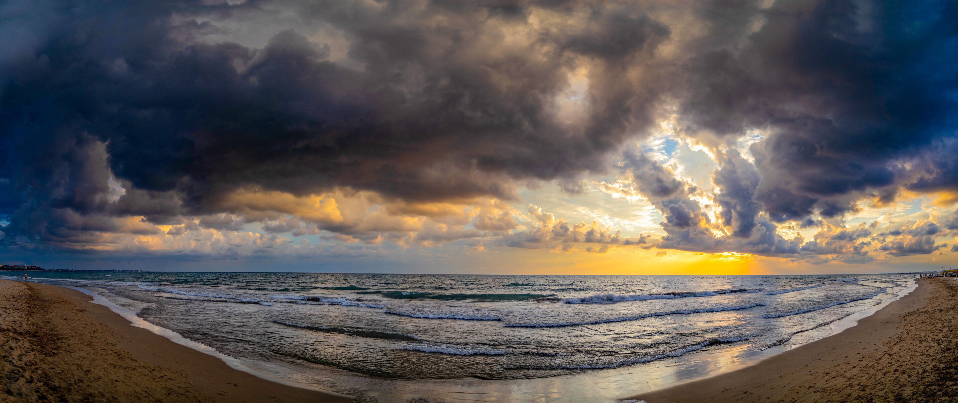 A beach with waves, a sunset, and a cloudy sky.