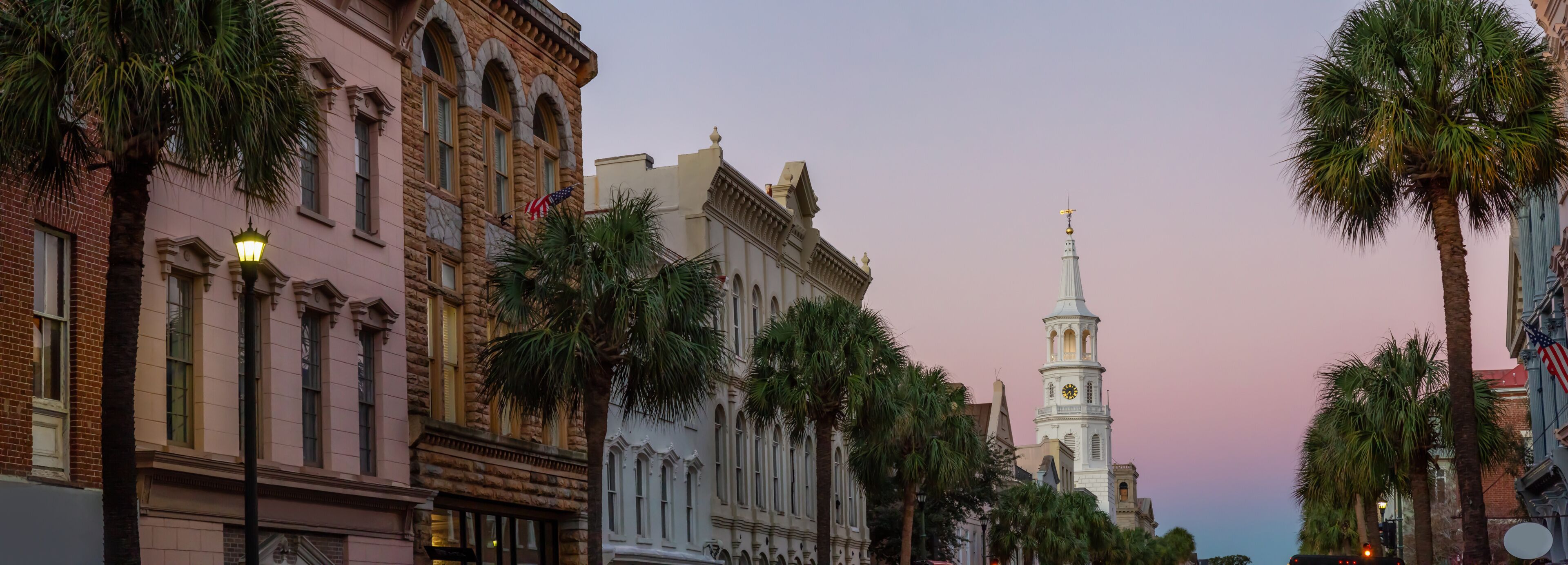 A street lined with historic buildings, palm trees, and a church tower with a clock.