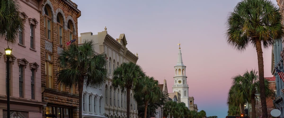 A street lined with historic buildings, palm trees, and a church tower with a clock.
