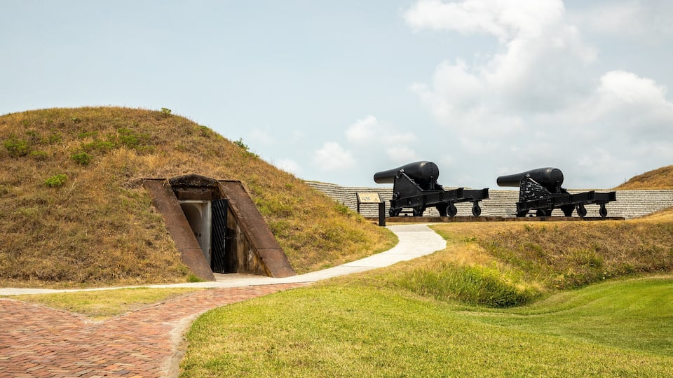 A historical site with cannons, a brick pathway, and a grassy hill.