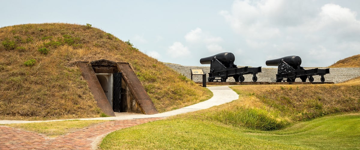 A historical site with cannons, a brick pathway, and a grassy hill.