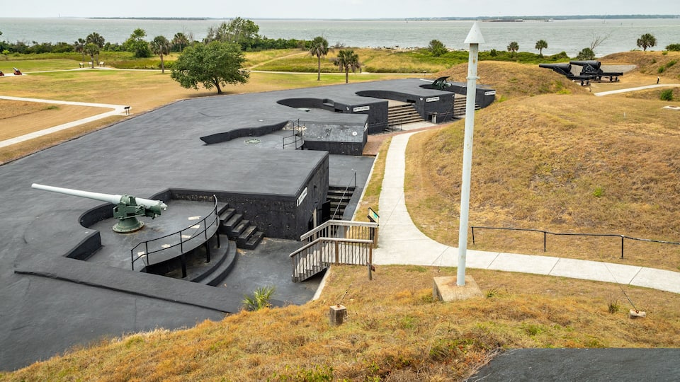 A coastal military site with cannons, a lighthouse, and a view of the ocean.