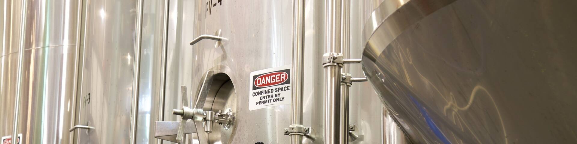 Stainless steel industrial tanks with safety warning signs.