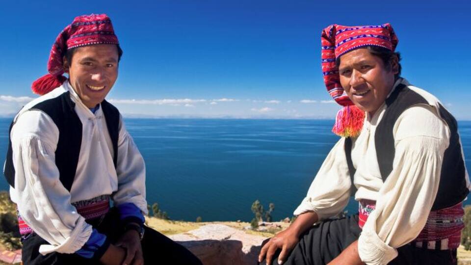 Two people in traditional attire sitting on a cliff overlooking a vast ocean.