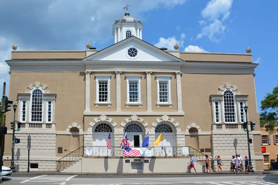 Un bâtiment historique doté d’une tour horlogée, de fenêtres en arc et de drapeaux.