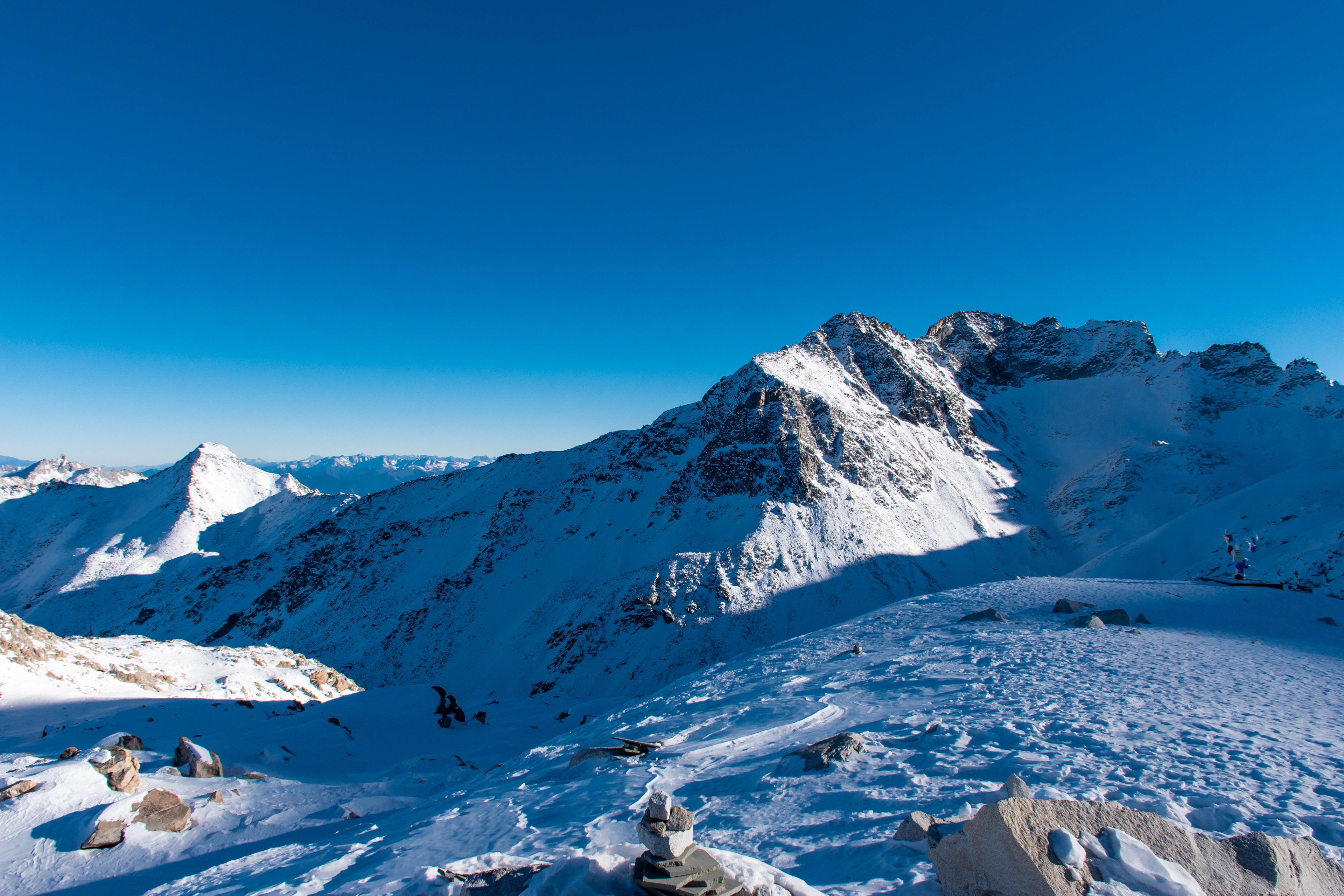 A snow-covered mountain range with sharp peaks and rocky outcrops under a clear blue sky.