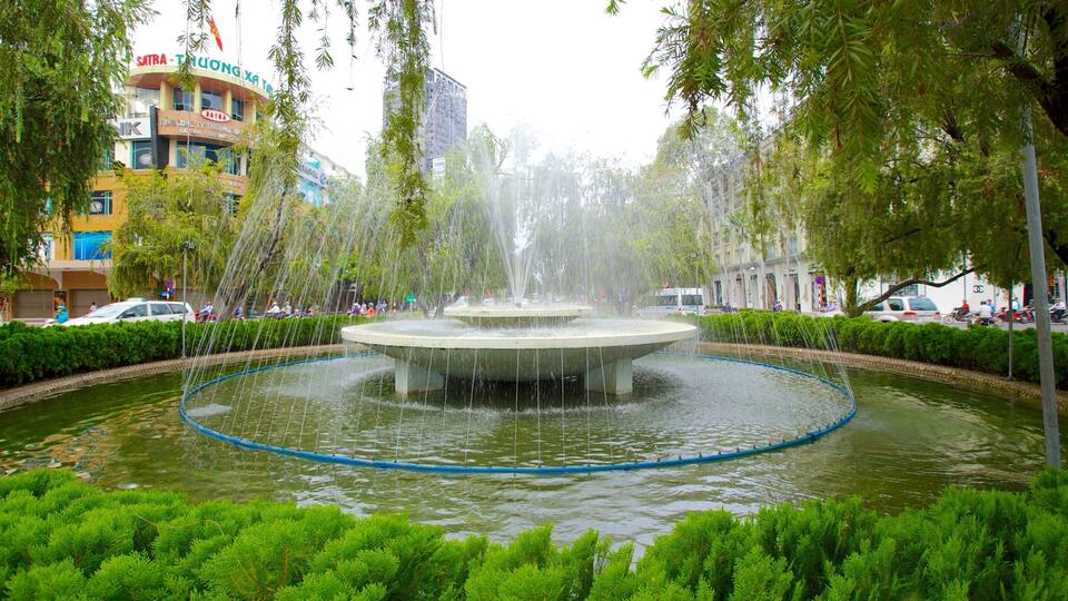 A fountain surrounded by greenery and buildings.