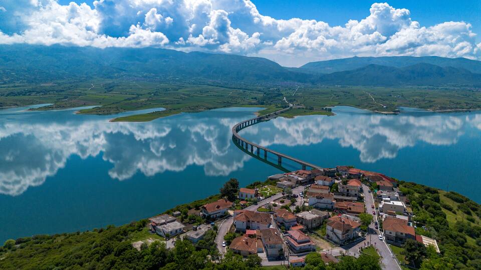 A coastal town with a bridge over a lake, surrounded by mountains and greenery.