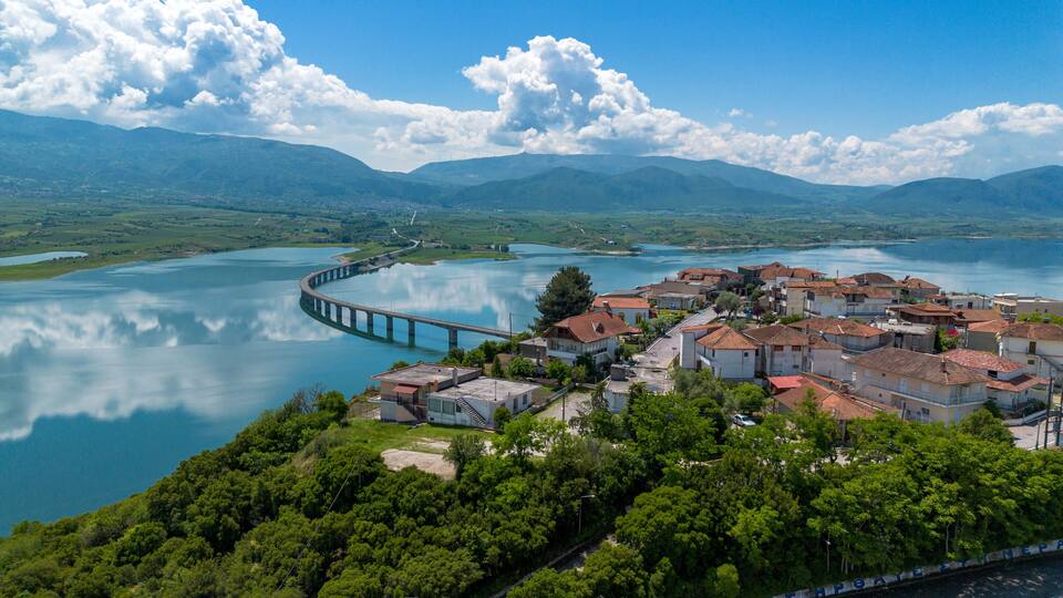 A coastal town with a bridge over a calm lake, surrounded by mountains.
