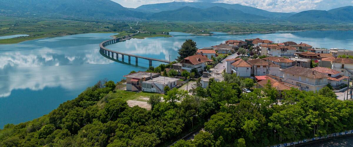 A coastal town with a bridge over a calm lake, surrounded by mountains.