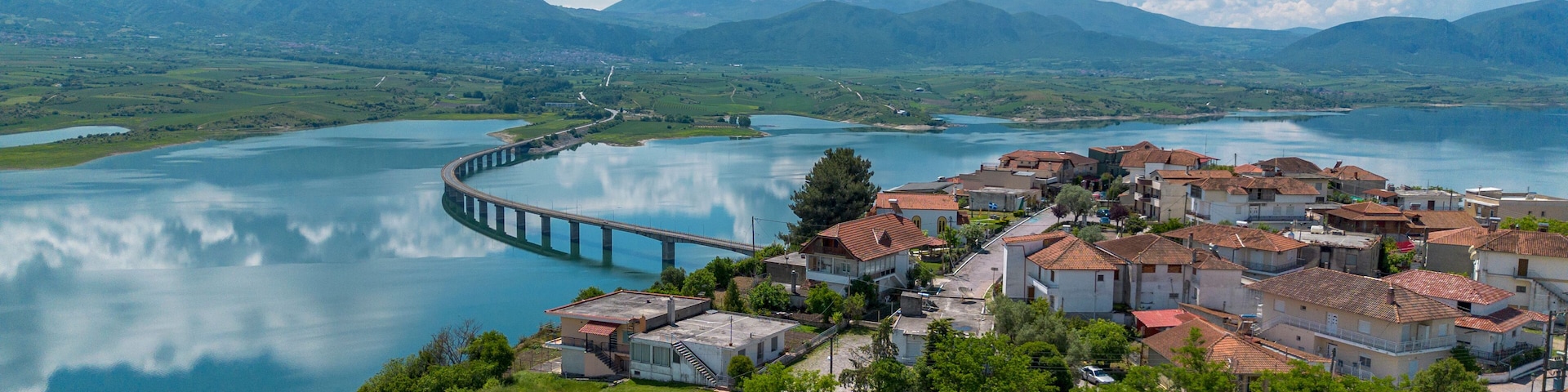 A coastal town with a bridge over a calm lake, surrounded by mountains.