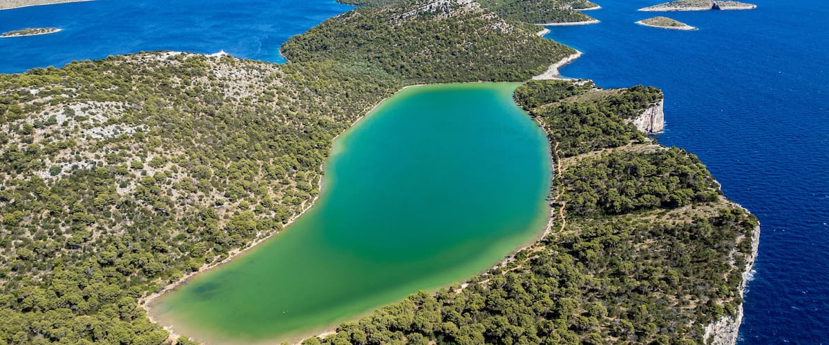 Aerial view of the saltwater Lake Mir in Telascica Nature Park, surrounded by pine forests and cliffs overlooking the Adriatic Sea in Sali, Zadar County, Croatia.