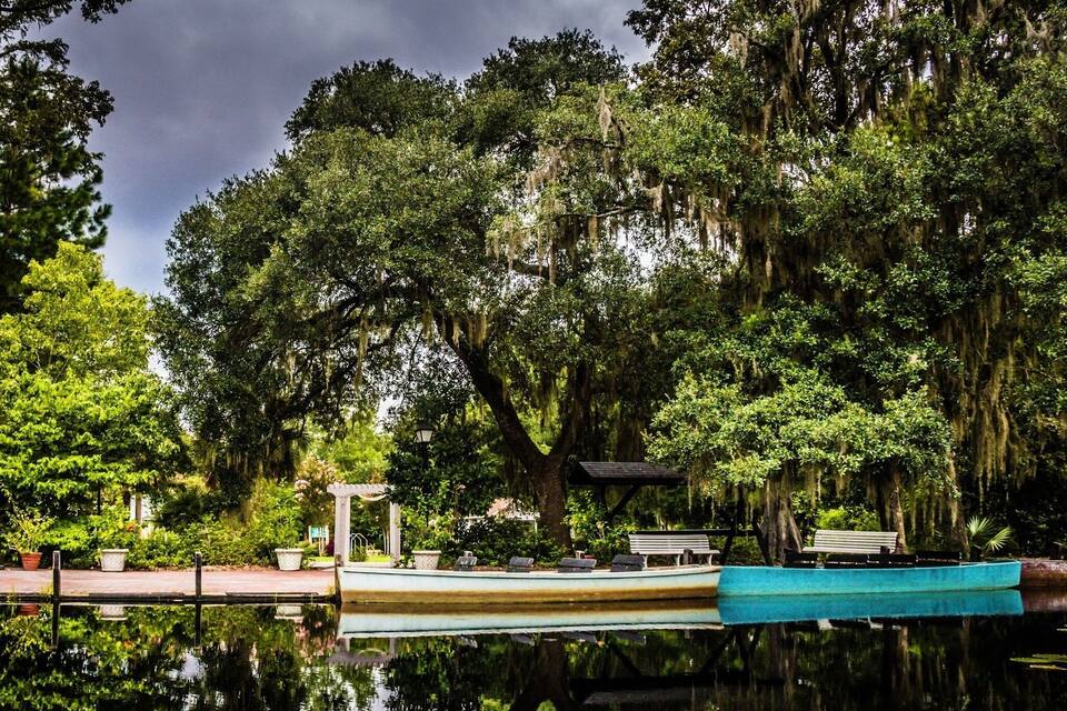 A calm lake with a boat docked on the shore, surrounded by lush greenery and large trees with hanging moss.