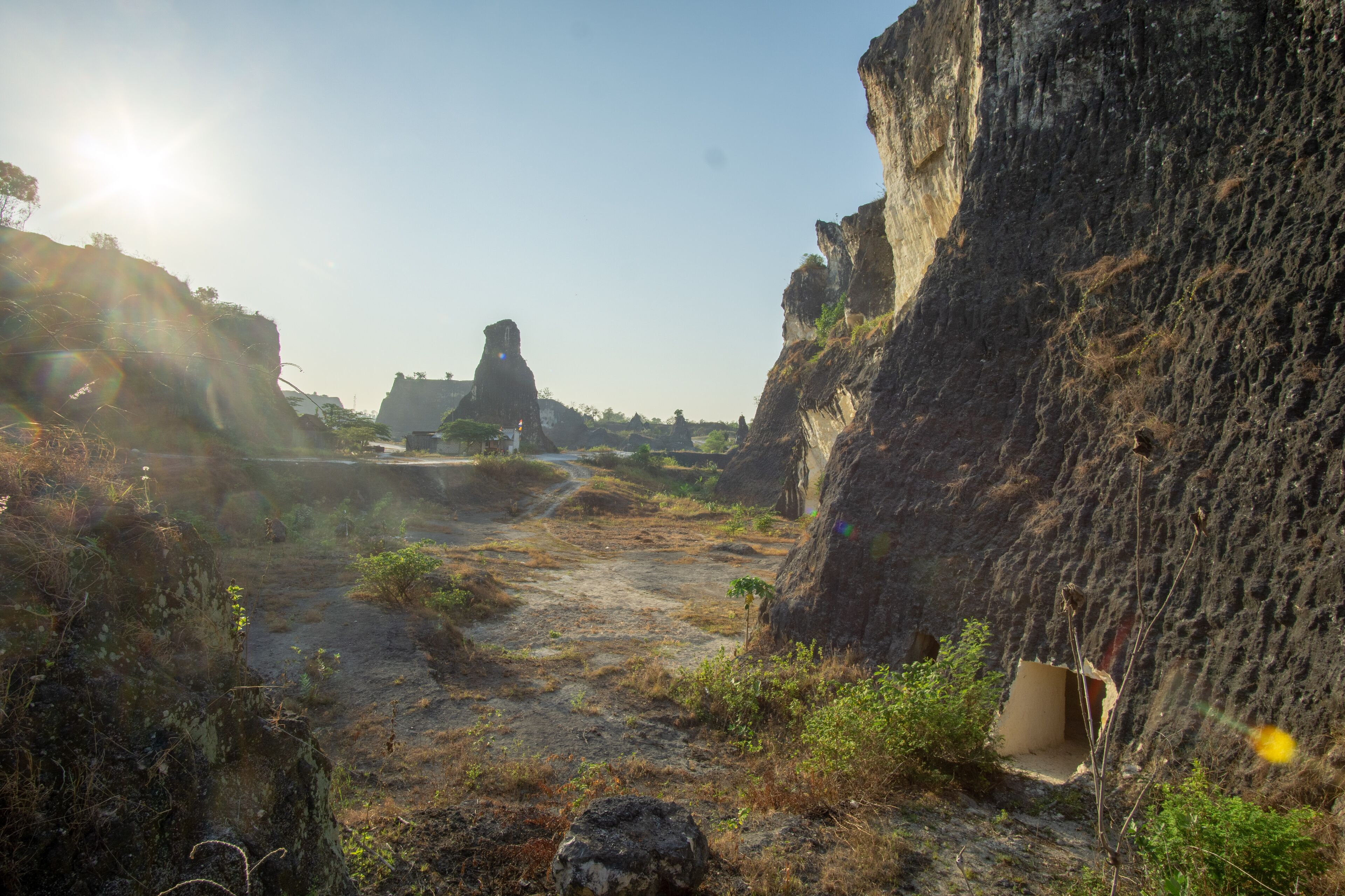 A rocky landscape with a narrow path, large rock formations, and a distant structure.