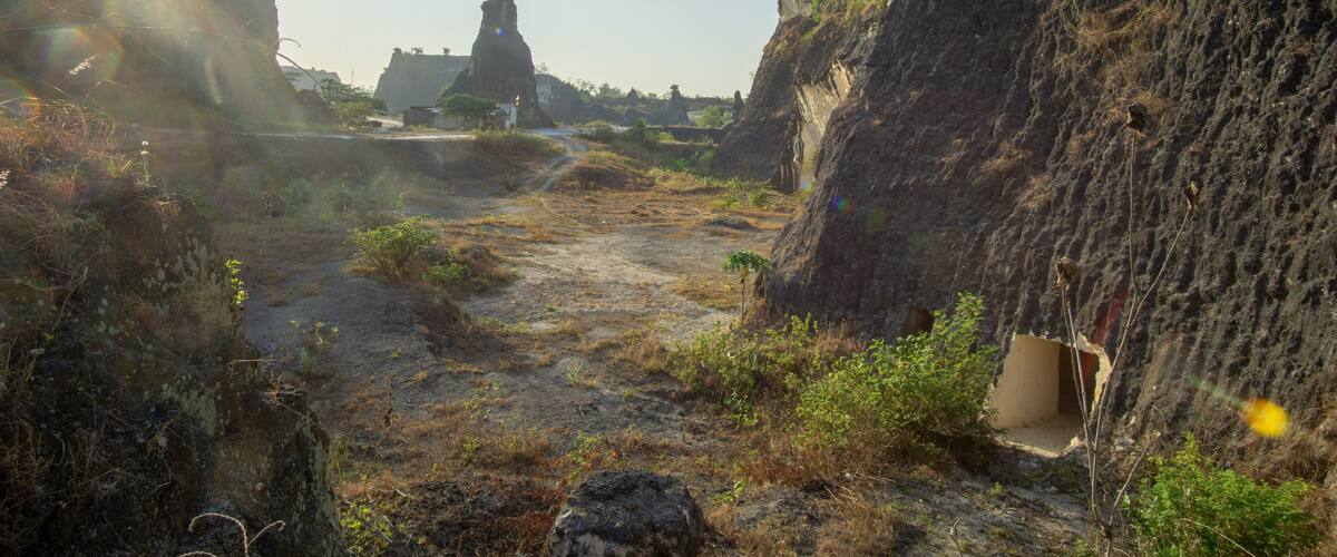 A rocky landscape with a narrow path, large rock formations, and a distant structure.