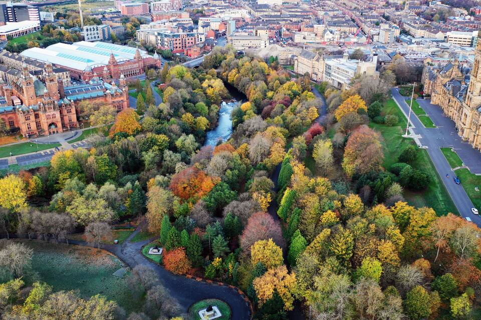An aerial view of a city with a river, historic buildings, and autumn foliage.