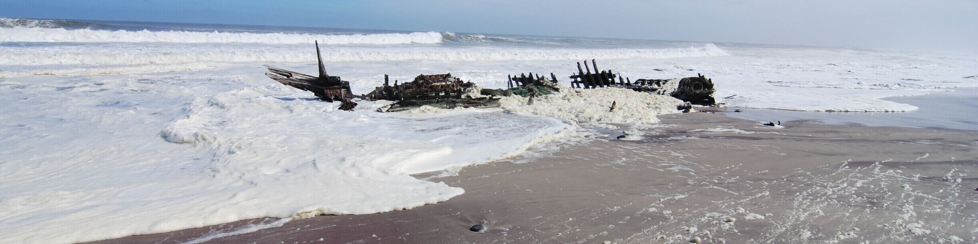 Uma praia congelada com destroços espalhados e ondas quebrando na costa.