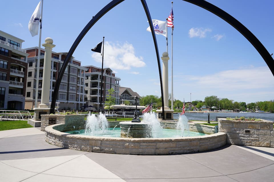 A waterfront fountain with American flags, surrounded by a stone structure and a clear blue sky.