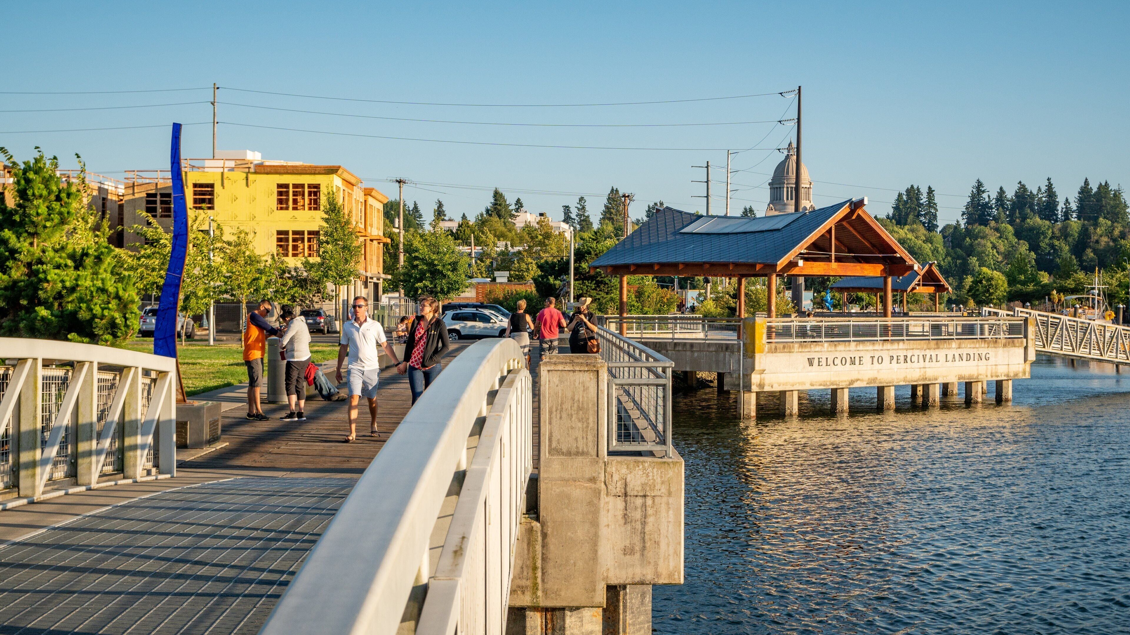 Een voetgangersbrug over water met een houten kiosk en een bord waarop staat: "WELCOME TO PERCIVAL LANDING".
