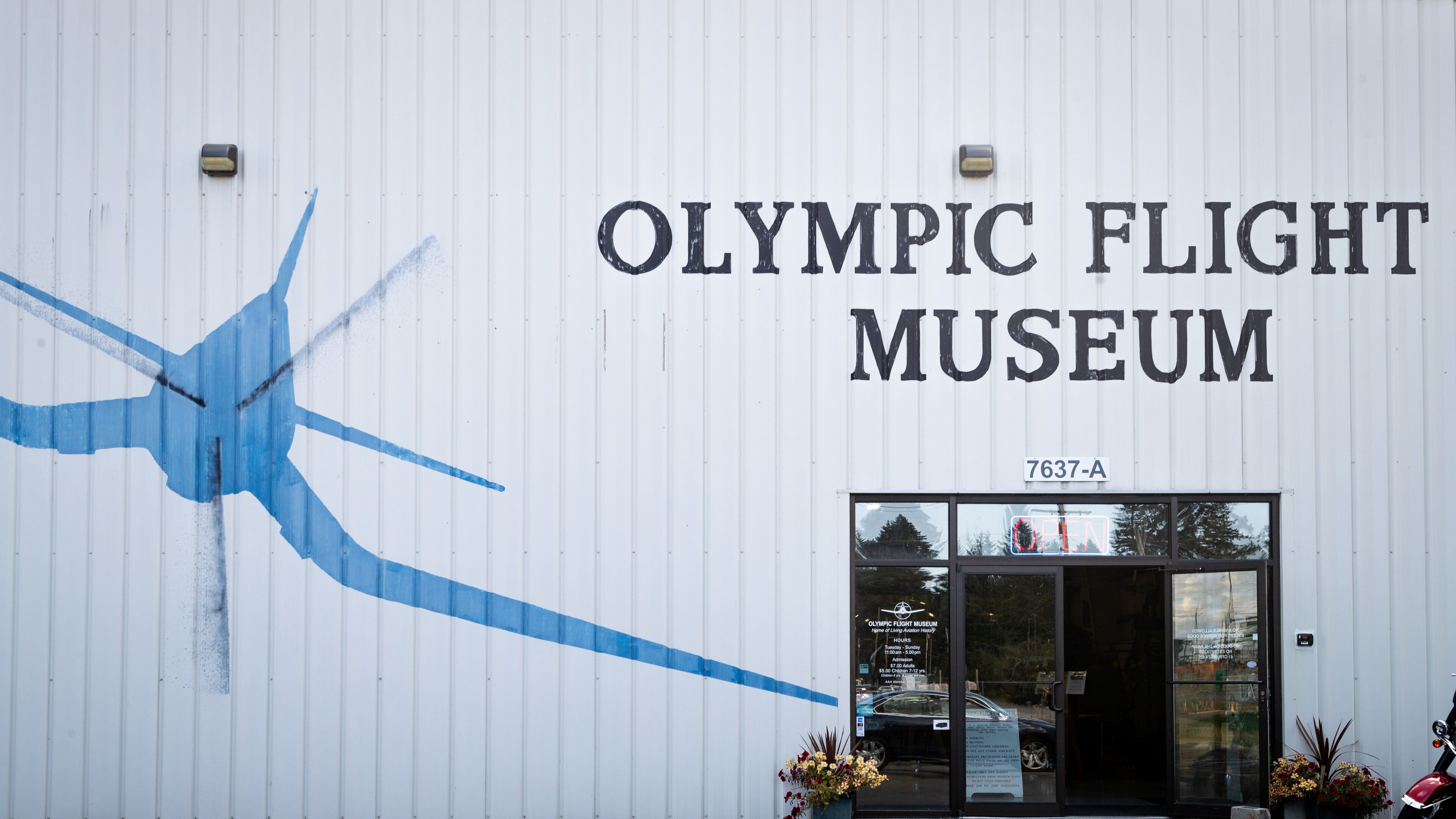 Exterior del Museo del Vuelo Olímpico, con un gran mural azul de un avión y el nombre del museo.