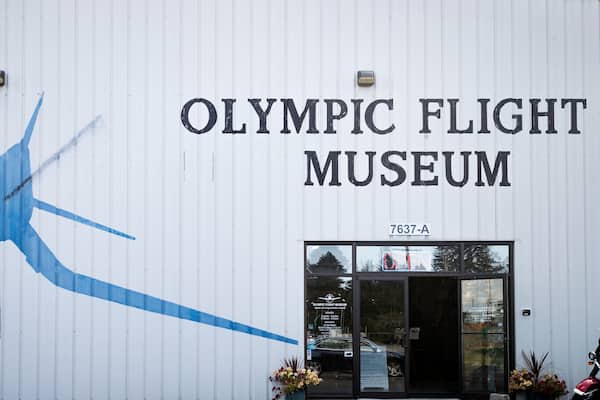 Exterior do Museu Olympic Flight com um grande mural de um avião azul e o nome do museu.