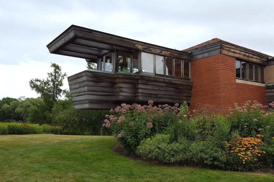 Et moderne hus med en træ tilbygning og en have med lyserøde og gule blomster.
