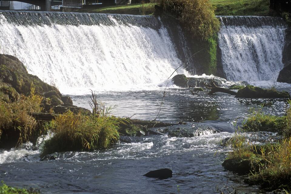 A river flowing over rocks with a waterfall in the background.
