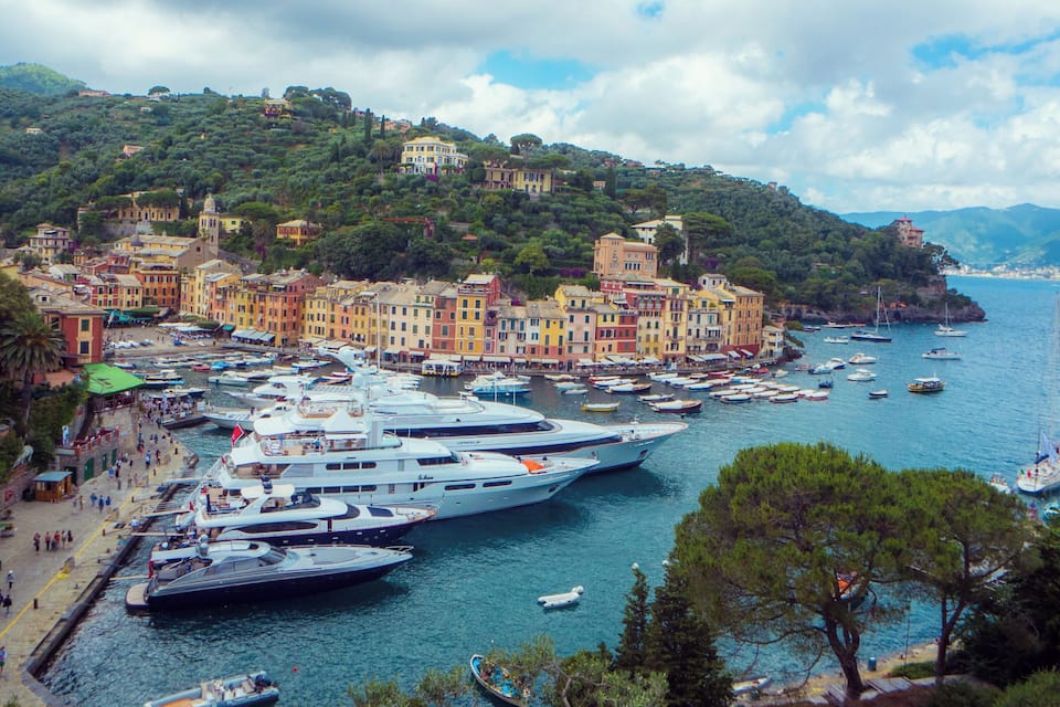 A coastal town with colorful buildings, a marina with yachts, and boats docked along the waterfront.