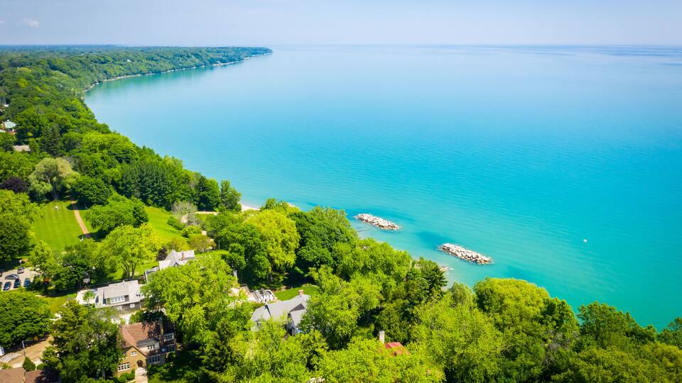 A coastal landscape with a turquoise lake, dense green trees, and a small pier.