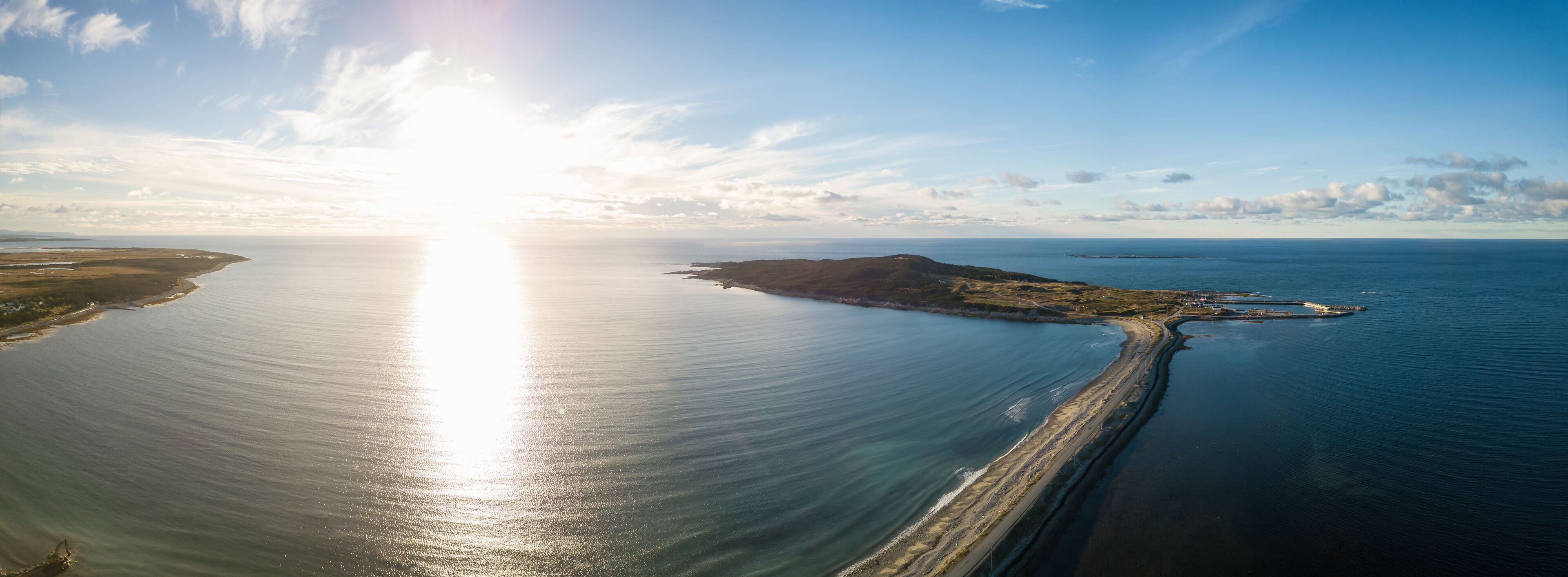 A coastal landscape with a sunlit sea, a sandy beach, and a small island with a lighthouse.