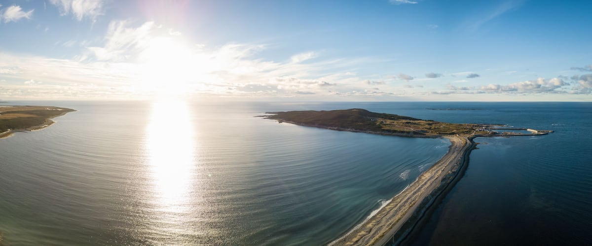 A coastal landscape with a sunlit sea, a sandy beach, and a small island with a lighthouse.