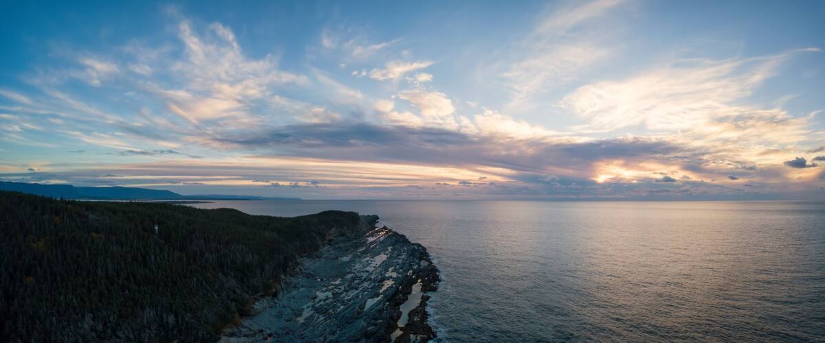 Un paisaje costero con costa rocosa, bosque denso y mar tranquilo bajo un cielo parcialmente nublado.