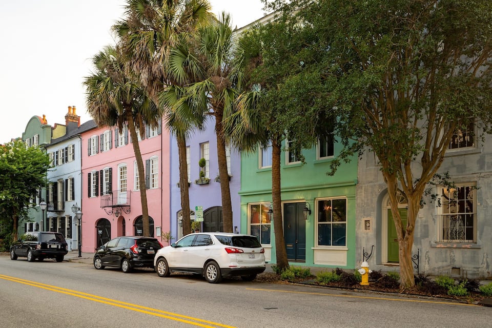 A street lined with colorful buildings, parked cars, and trees.