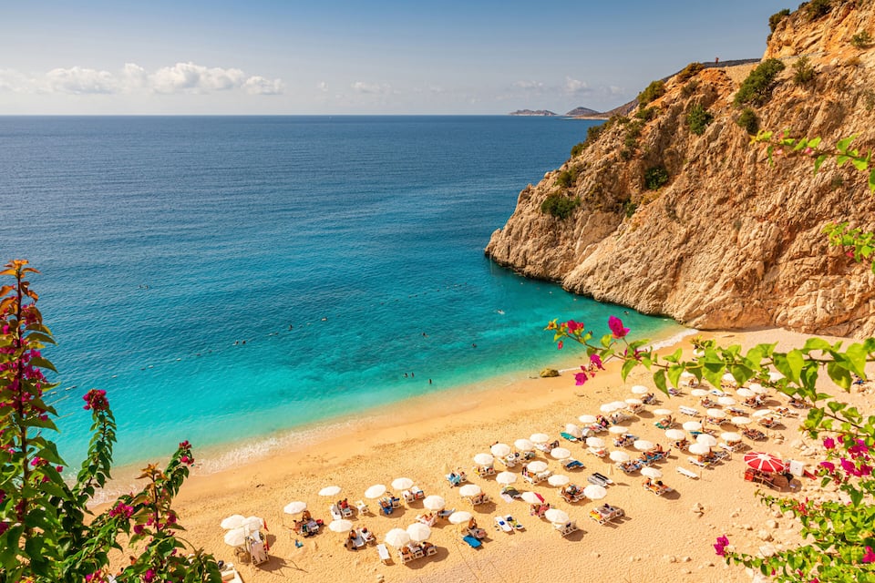Une plage côtière aux eaux turquoise et limpides, bordée d’un rivage sablonneux et de falaises rocheuses.