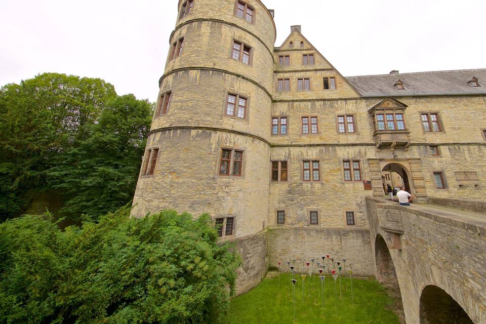 Eine historische Steinburg mit einem runden Turm, einer Bogenbrücke und üppiger Vegetation.