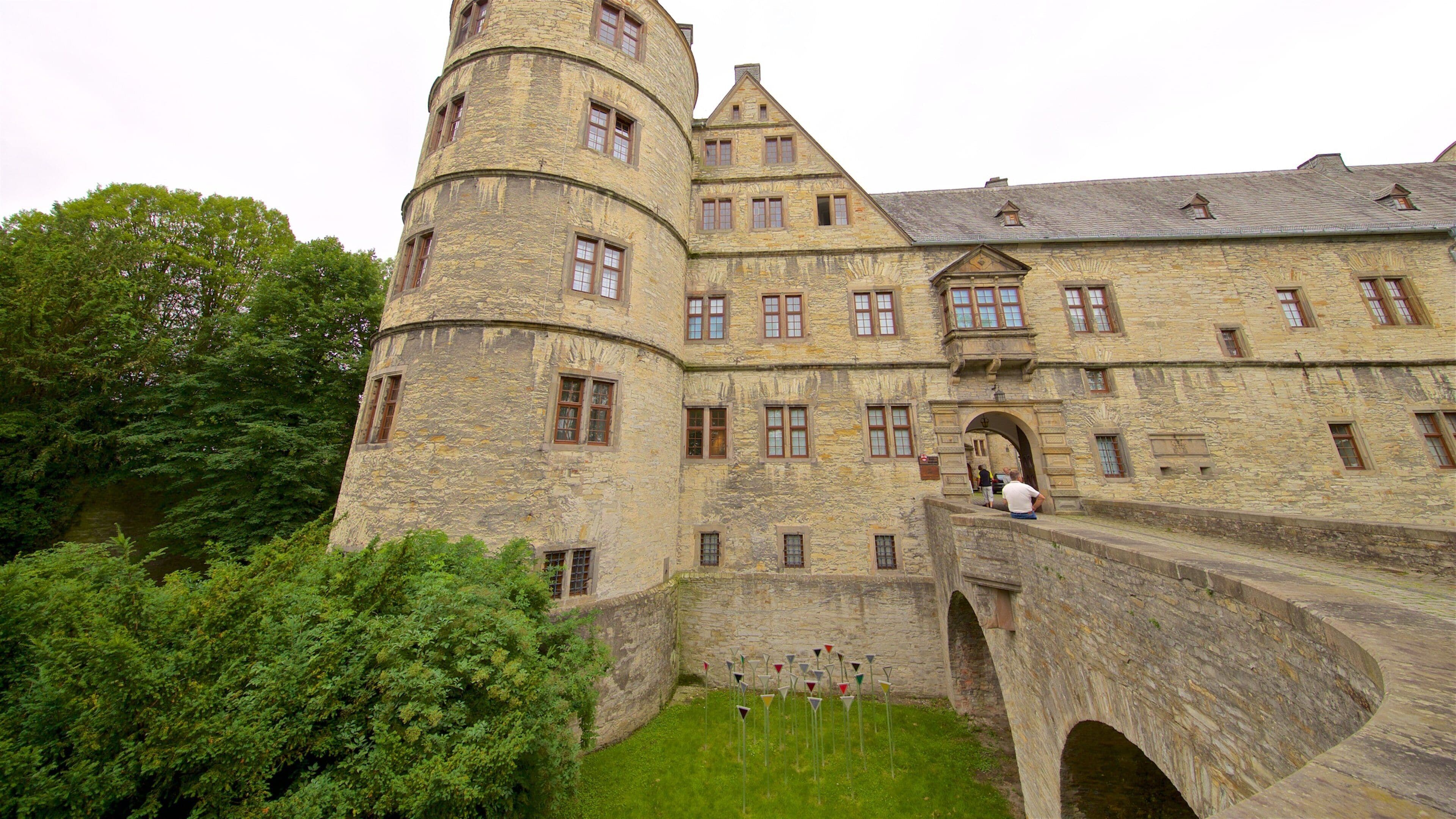 A historic stone castle with a round tower, arched bridge, and lush greenery.
