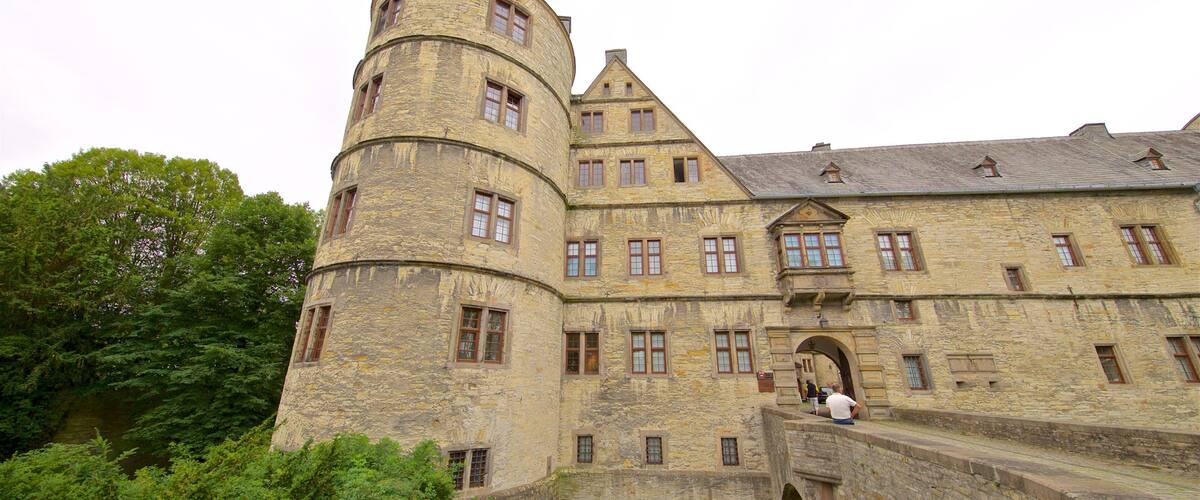 A historic stone castle with a round tower, arched bridge, and lush greenery.