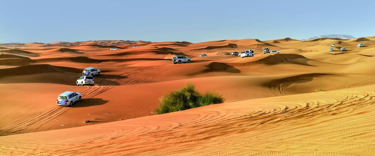 A desert landscape with white vehicles navigating the sand dunes.