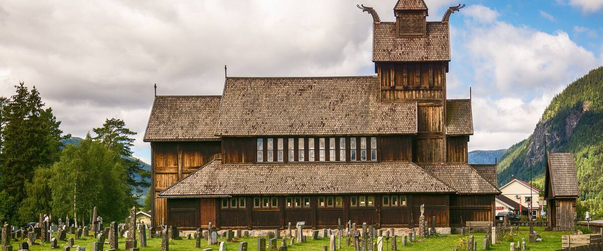 A wooden church with a steeply pitched roof and a spire, surrounded by a cemetery with numerous gravestones.