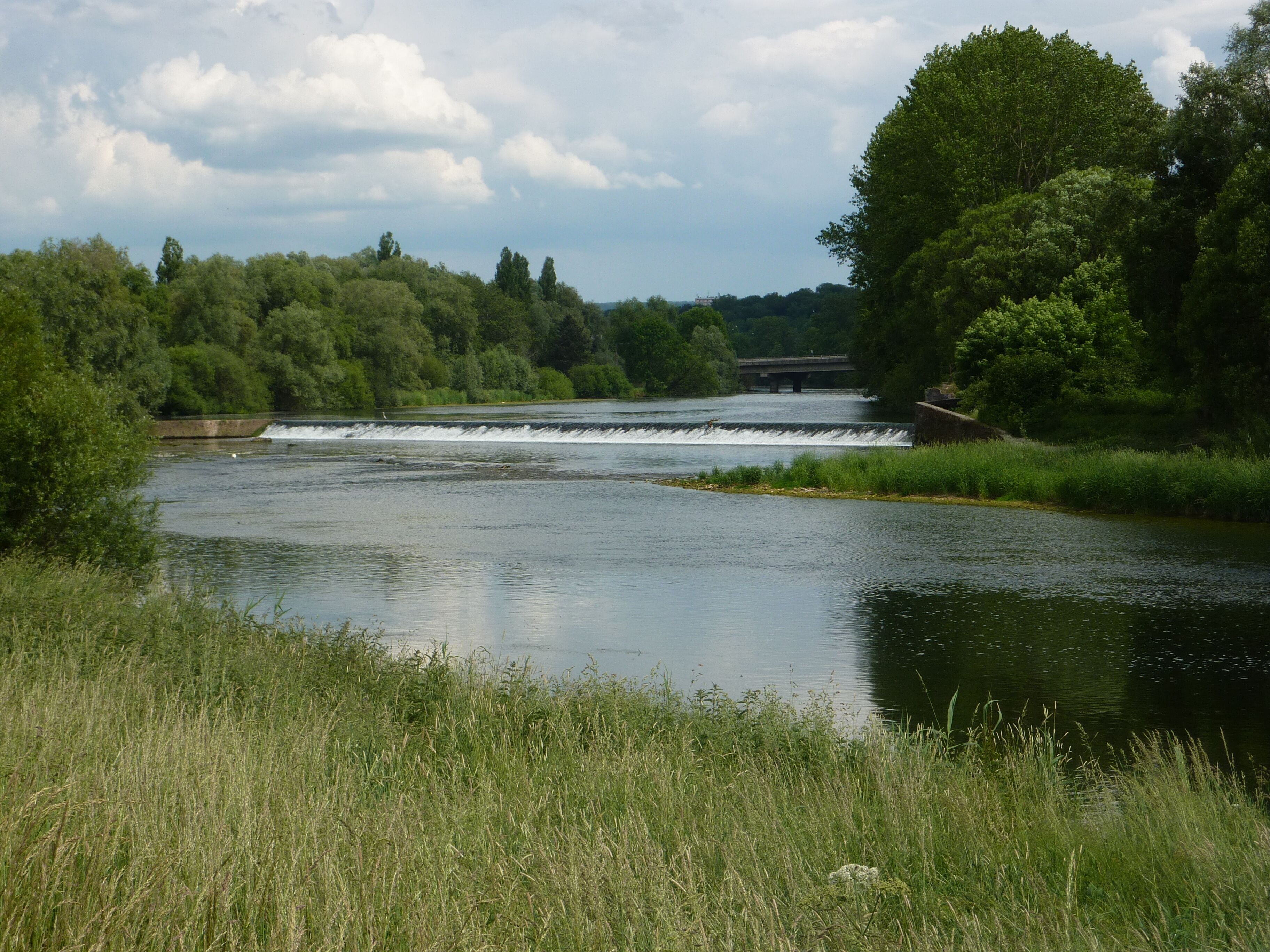 A river with a dam and a bridge in the background.
